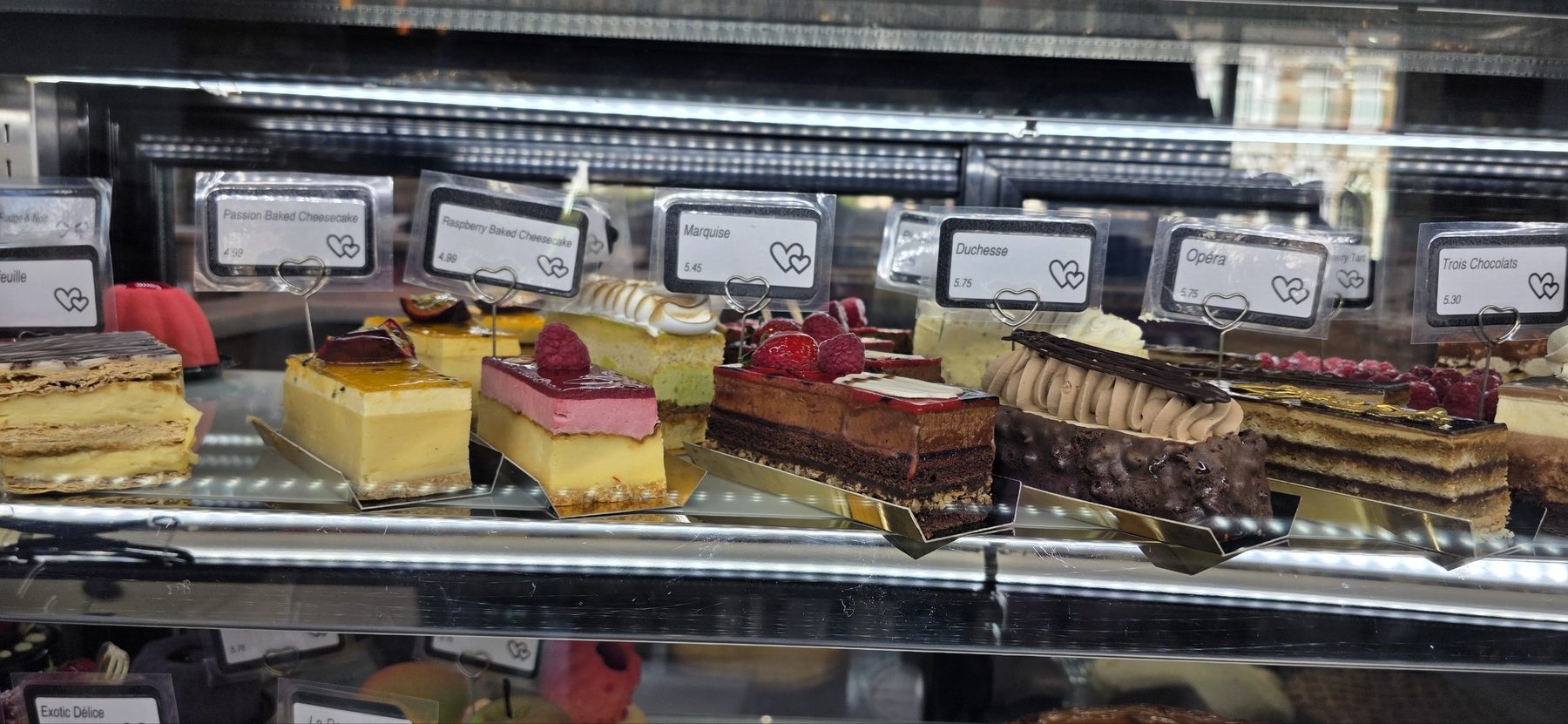 A row of cake slices in the counter: mille-feuille, passion cheesecake, Marquise, Duchesse, Opéra and Trois Chocolats