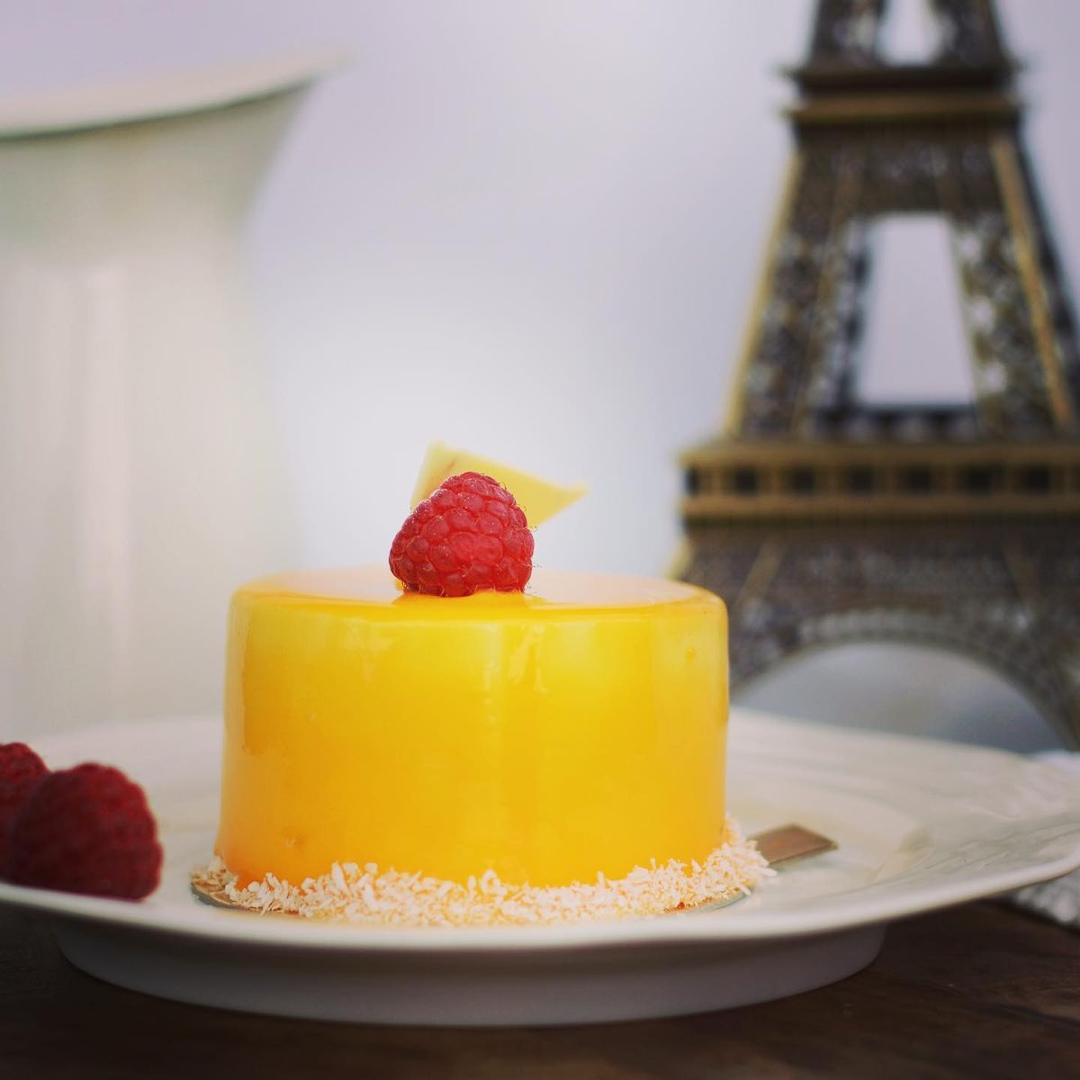 Exotic Délice mousse cake with a mirror glaze, beside a small Eiffel Tower