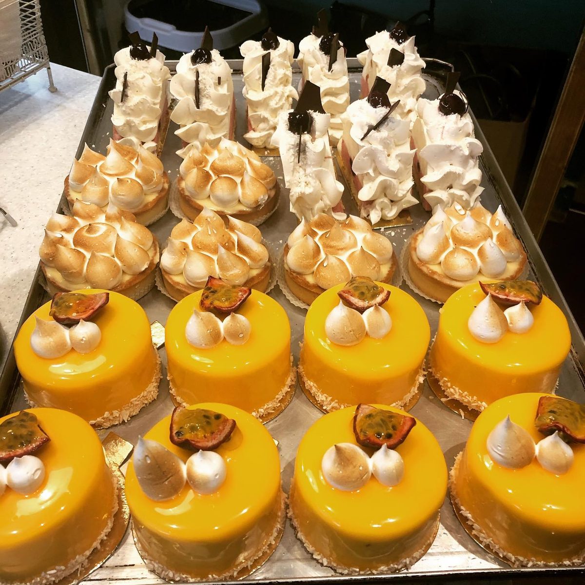 Trays of lemon meringue tarts and mango entremets ready for the counter