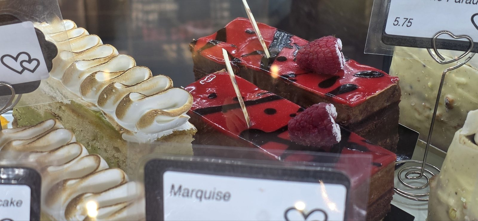 Marquise slices with a red mirror glaze and raspberries, beside pistachio meringue tarts