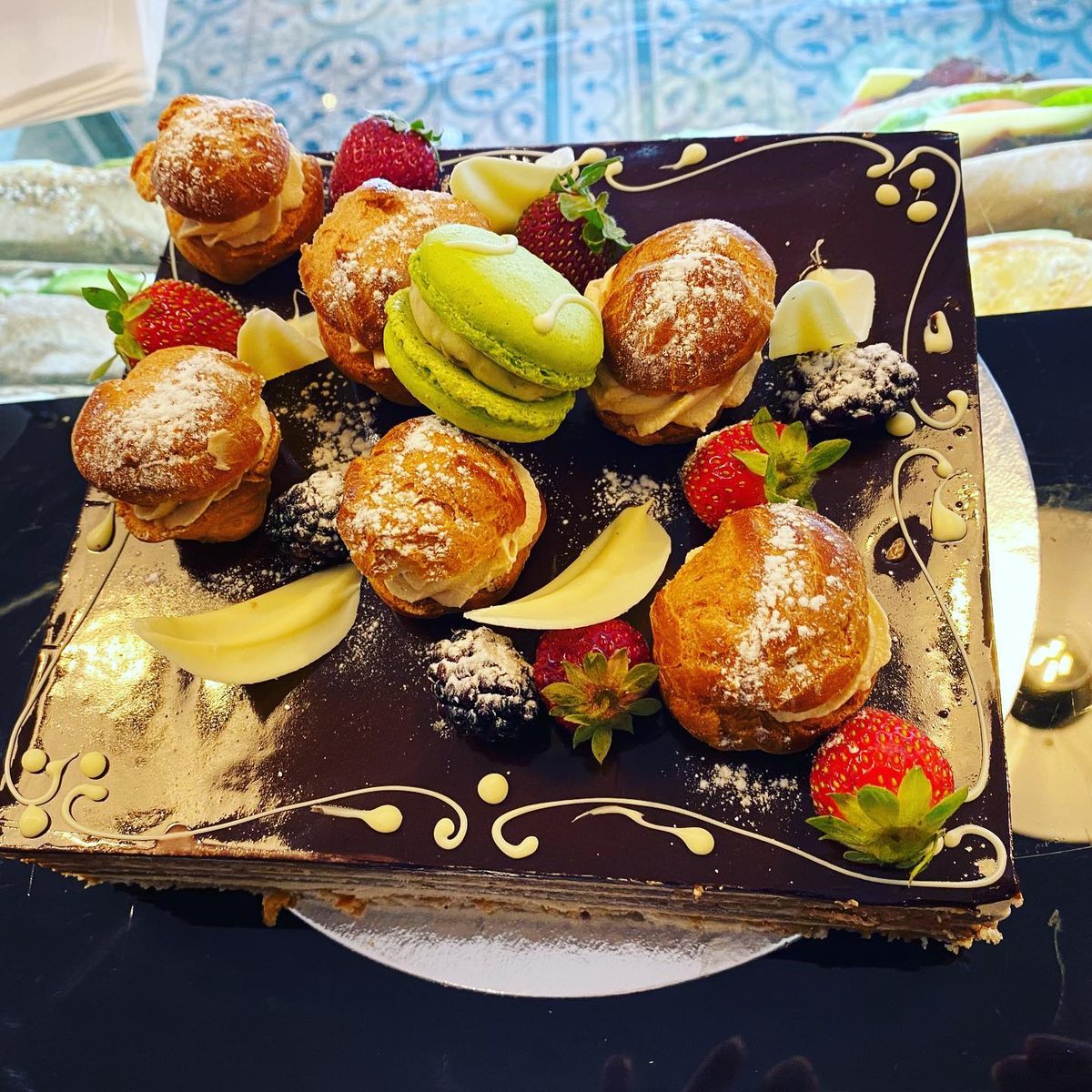 A large chocolate mille-feuille topped with choux buns, macarons and fresh berries