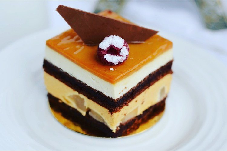 A layered pear and caramel entremet with a chocolate shard and dusted raspberry